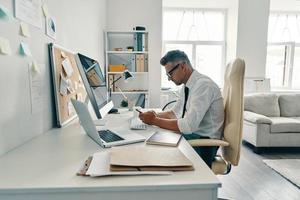 Always available. Thoughtful young man in shirt and tie using smart phone while sitting in the office photo