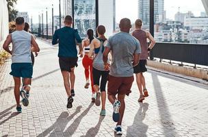 vista trasera de personas con ropa deportiva corriendo mientras hacen ejercicio en la acera al aire libre foto