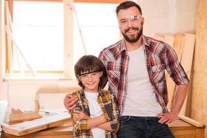 mi seguidor profesional. alegre joven carpintero abrazando a su hijo mientras está de pie en el taller foto