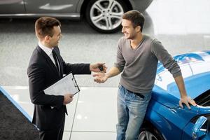 buen negocio. vista de ángulo alto del vendedor de autos joven haciendo trato con el cliente en el concesionario foto