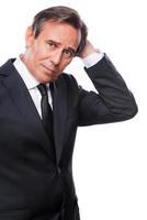 Lost in thoughts. Worried mature man in formalwear holding hand in hair and looking at camera while standing isolated on white background photo