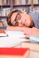 estudiante durmiendo. apuesto joven durmiendo mientras está sentado en la biblioteca y apoyando su rostro en el escritorio foto