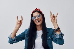 mujer joven atractiva en bandana gesticulando y sonriendo mientras está de pie contra el fondo gris foto