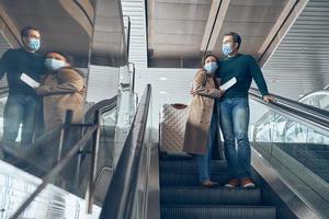 pareja madura que lleva boletos mientras se mueve por una escalera mecánica en la terminal del aeropuerto foto