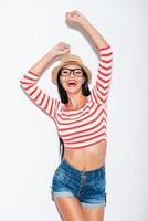 She likes her funky style. Playful young woman keeping arms raised while standing against white background photo