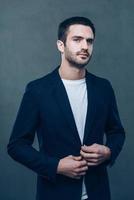 Used to look good. Handsome young man adjusting his jacket and looking at camera while standing against grey background photo