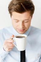 Smelling a fresh coffee. Handsome young man in shirt and tie smelling coffee and keeping eyes closed while holding a cup of coffee near face photo