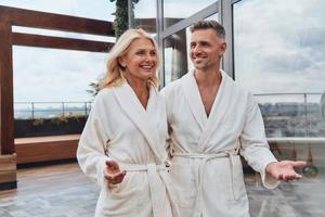 Beautiful mature couple in bathrobes enjoying fruits and wine while relaxing in luxury hotel outdoors photo