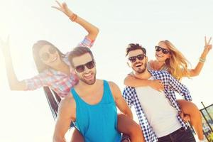 Youthful fun. Low angle view of two cheerful young men carrying their girlfriends on the shoulders while having fun on the roof photo