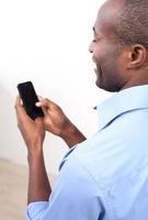 Typing a message. Rear view of cheerful black man typing something on the mobile phone and smiling while standing isolated on grey photo