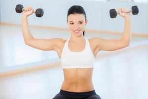 Young woman doing arm curls. Attractive young woman smiles as she performs arm curls with a set of dumbbells photo