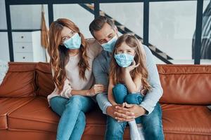 Young family with preschool age girl wearing protective face masks while bonding together at home photo