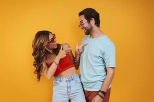 Beautiful young couple in eyeglasses having fun while standing against yellow background photo