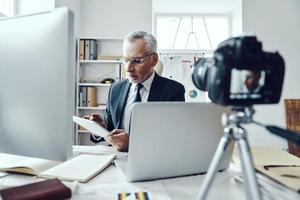 Senior man in elegant business suit using modern technologies while making social media video photo