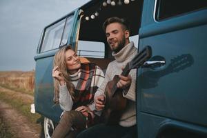 Song for her.  Handsome young man playing guitar for his beautiful girlfriend while sitting in blue retro style mini van photo