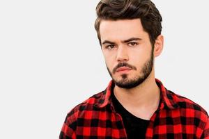 Suspicious glance. Serious young man looking at camera while standing against white background photo