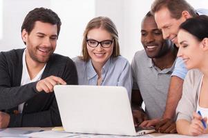 Creative team at work. Group of business people in casual wear sitting together at the table and discussing something while looking at the laptop photo