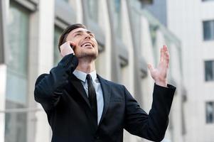 Good news. Cheerful young men in formalwear talking on the mobile phone and rise his hand up photo