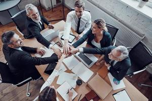 Top view of cheerful business team keeping hands together as a symbol of unity while working together in the modern office photo