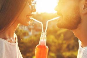 feliz pareja joven bebiendo de una botella con pajitas foto