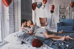 expresando amor verdadero. hermosa joven pareja abrazándose y sonriendo mientras está acostado en la cama en casa foto