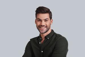 Simply happy. Handsome young man smiling and looking at camera while standing against grey background photo