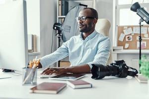 Handsome young African man using computer while working in the modern office photo