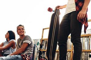 Friends make each other happy. Group of young modern people hanging out together while spending time at the skate park outdoors photo