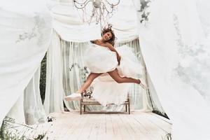 Celebrating her special day. Full length of attractive young woman in wedding dress and sports shoes smiling while jumping in the wedding pavilion outdoors photo
