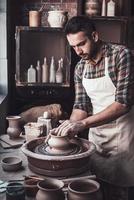 Confident and concentrated. Confident young man making ceramic pot on the pottery wheel photo