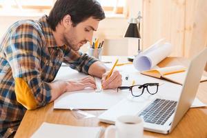 Getting to the point. Side view of concentrated young man working while sitting at his working place photo