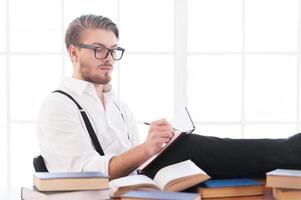 Writer at work. Handsome young man in shirt and suspenders writing something in notebook while sitting at his working place photo