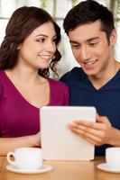 Surfing web together. Beautiful young loving couple sitting at the restaurant and using digital tablet photo