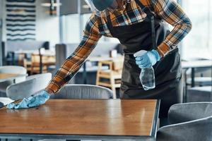 Close up of man in protective gloves cleaning table in restaurant photo