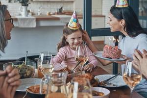 Happy family celebrating birthday of little girl while sitting at the dining table at home