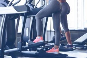 Step to beautiful body. Side view close-up part of young women working out on stepper at gym photo