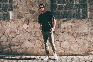 Cool and handsome. Full length of handsome young African man in casual clothes standing against the stoned wall outdoors photo