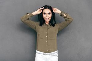 sentirse sorprendido. mujer joven atractiva con ropa informal elegante de pie contra un fondo gris y mirando sorprendida foto