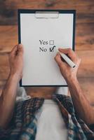 It is no. Top view of man making a check mark in clipboard while standing on the wooden floor photo