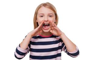 Happy little girl. Cheerful little girl shouting and holding hands near mouth while standing isolated on white photo