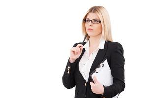 Looking for solution. Thoughtful mature businesswoman holding clipboard and touching her chin with pen while standing isolated on white photo