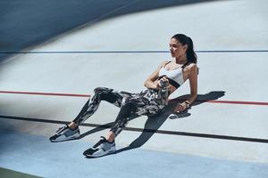 tomando un descanso. vista superior de una mujer joven con ropa deportiva relajándose mientras está en la pista de atletismo al aire libre foto