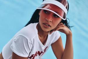 She will melt your heart.  Attractive young mixed race woman in swimwear looking away while sitting on the poolside photo