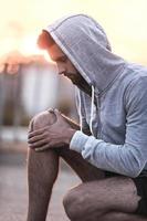 Massaging his injured knee. Side view of young man massaging knee while sitting outdoors photo