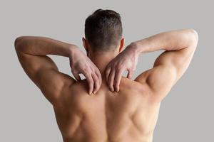 Muscular man. Rear view of young muscular man touching his shoulders while standing isolated on grey background photo