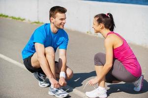 Getting ready for jogging. Top view of young man and woman tying shoelaces and looking at each other while being outdoors photo