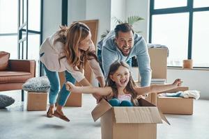 alegre familia joven sonriendo y desempacando sus cosas mientras se muda a un nuevo apartamento foto