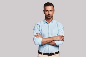 Positively charming. Handsome young man looking at camera while standing against grey background photo