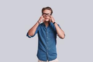 Just a little tired.  Handsome young man touching his eyes with fingers while standing against grey background photo