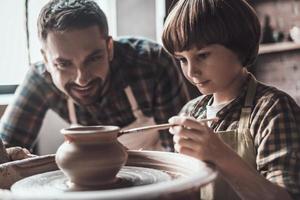 He got creative mind. Little boy drawing on ceramic pot at the pottery class while man in apron standing close to him and smiling photo